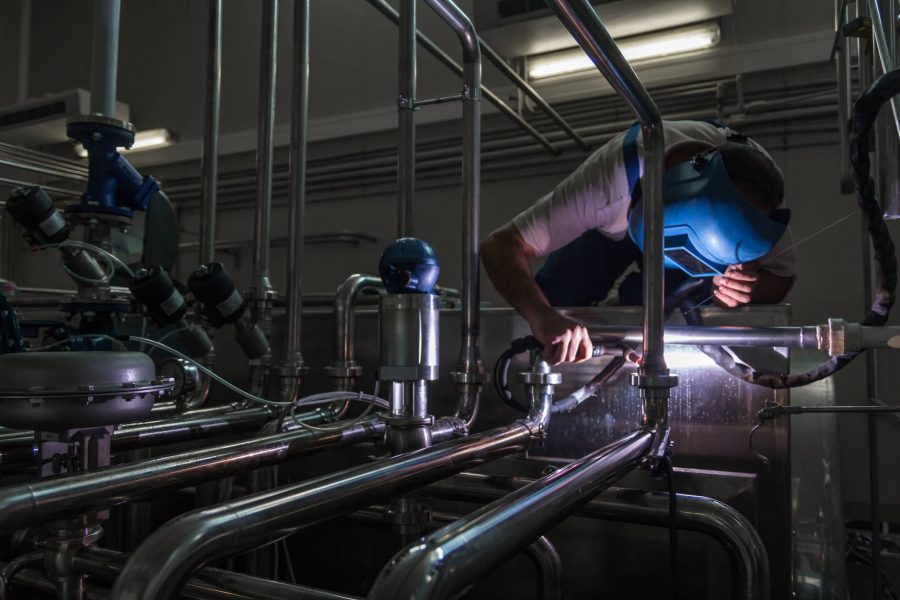 Man working and welding stainless steel pipes in a dairy factory.